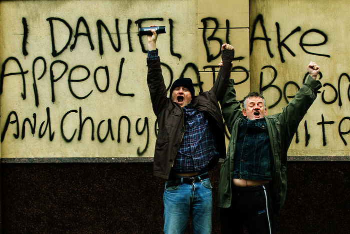 Nach einem weiteren frustrierenden Vorsprechen beim Amt greift Daniel Blake (Dave Johns, links) schließlich zu drastischen Mitteln um sich Gehör zu verschaffen. Er sprüht seine Forderung auf Widerrufung auf die Außenwand des Amtes. Für seine Courage wird er von einem vorbeigehenden Passanten als Held gefeiert. Bild: Sender / ZDF / Joss Barratt